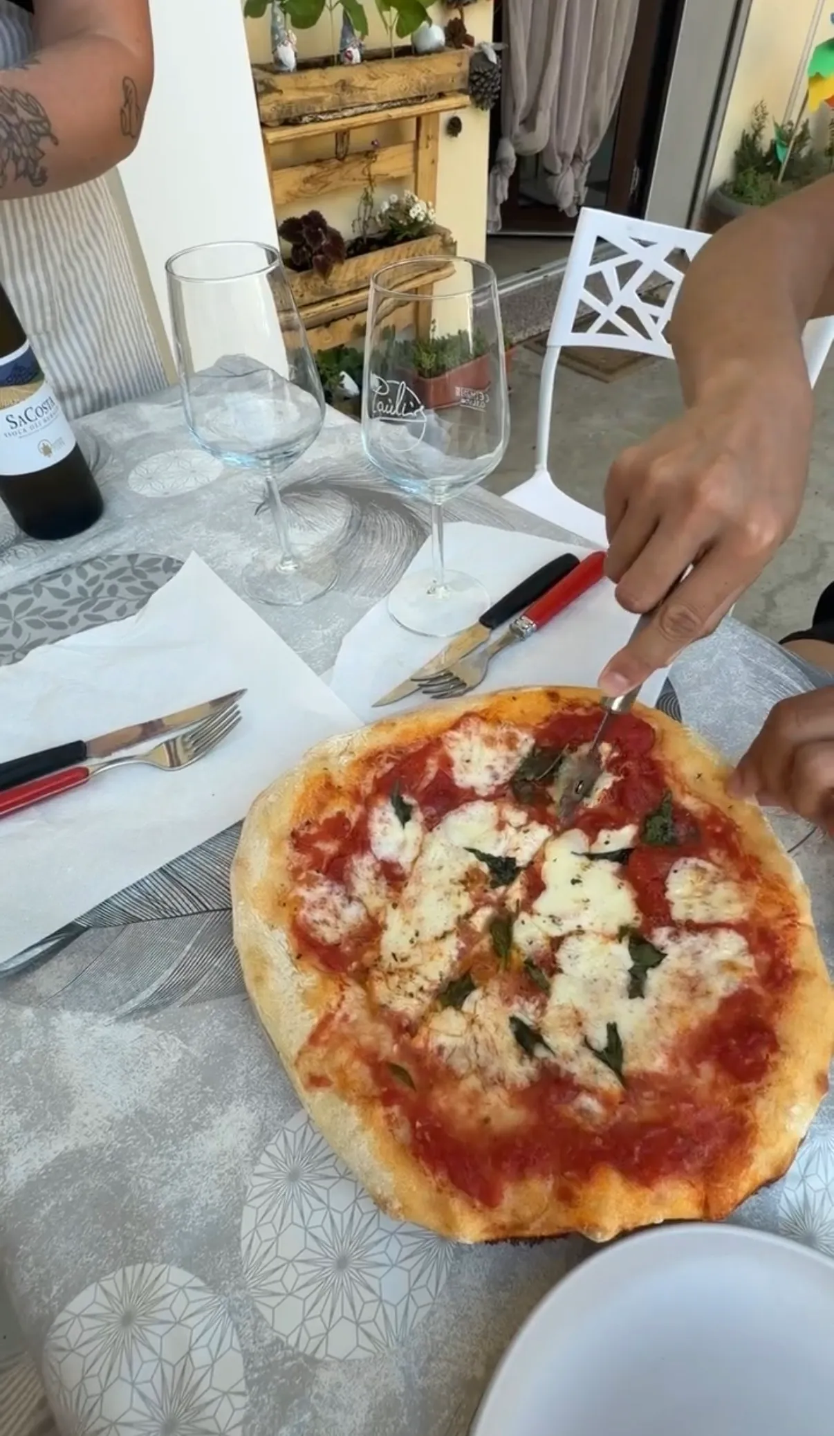 Cutting into a homemade margherita pizza with wine at a home pizza making class near Cagliari.