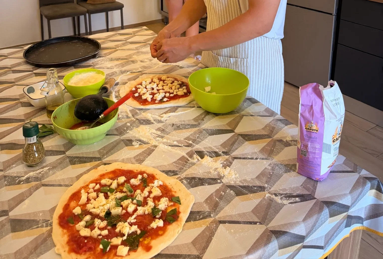 Topping homemade pizza dough with tomato sauce and fresh mozzarella at a home pizza making class in Cagliari.